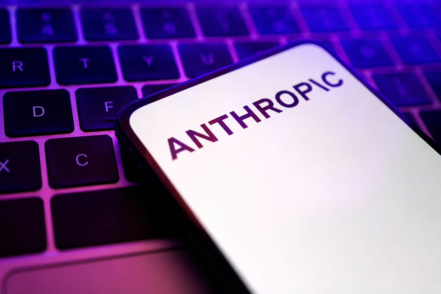 Close-up of a smartphone screen showing the word ANTHROPIC resting on a backlit keyboard with purple lighting.