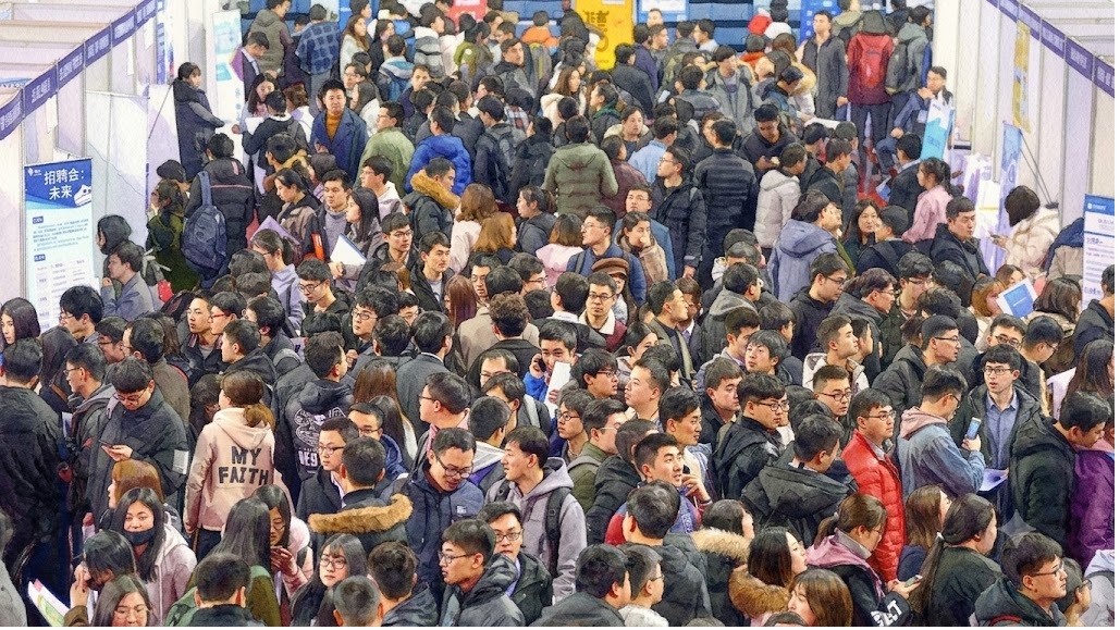 Very crowded convention or job fair hall with attendees walking between booths and holding papers.