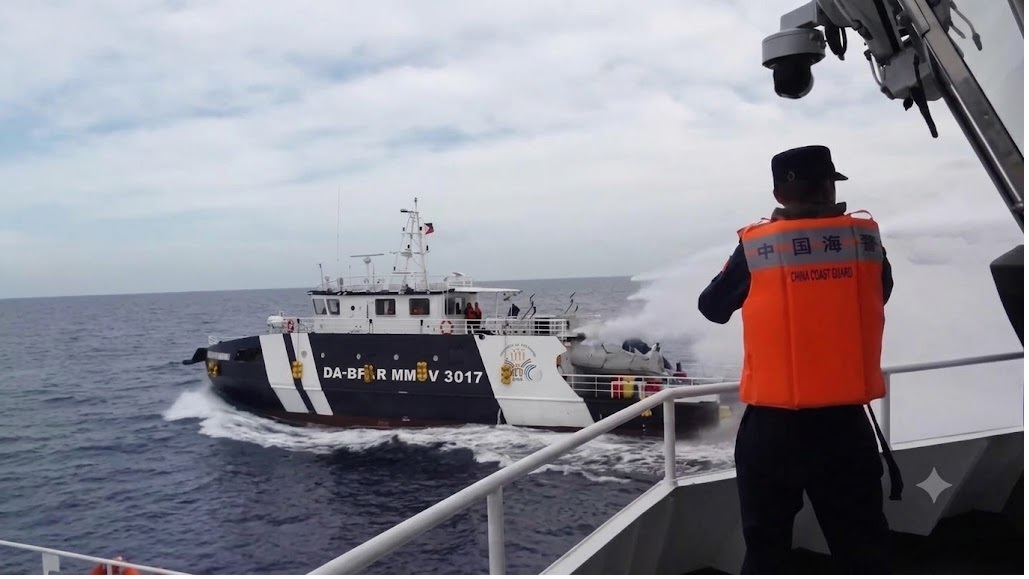 China Coast Guard officer in an orange life vest on a deck, watching a black-and-white patrol vessel spraying water as they sail at sea.